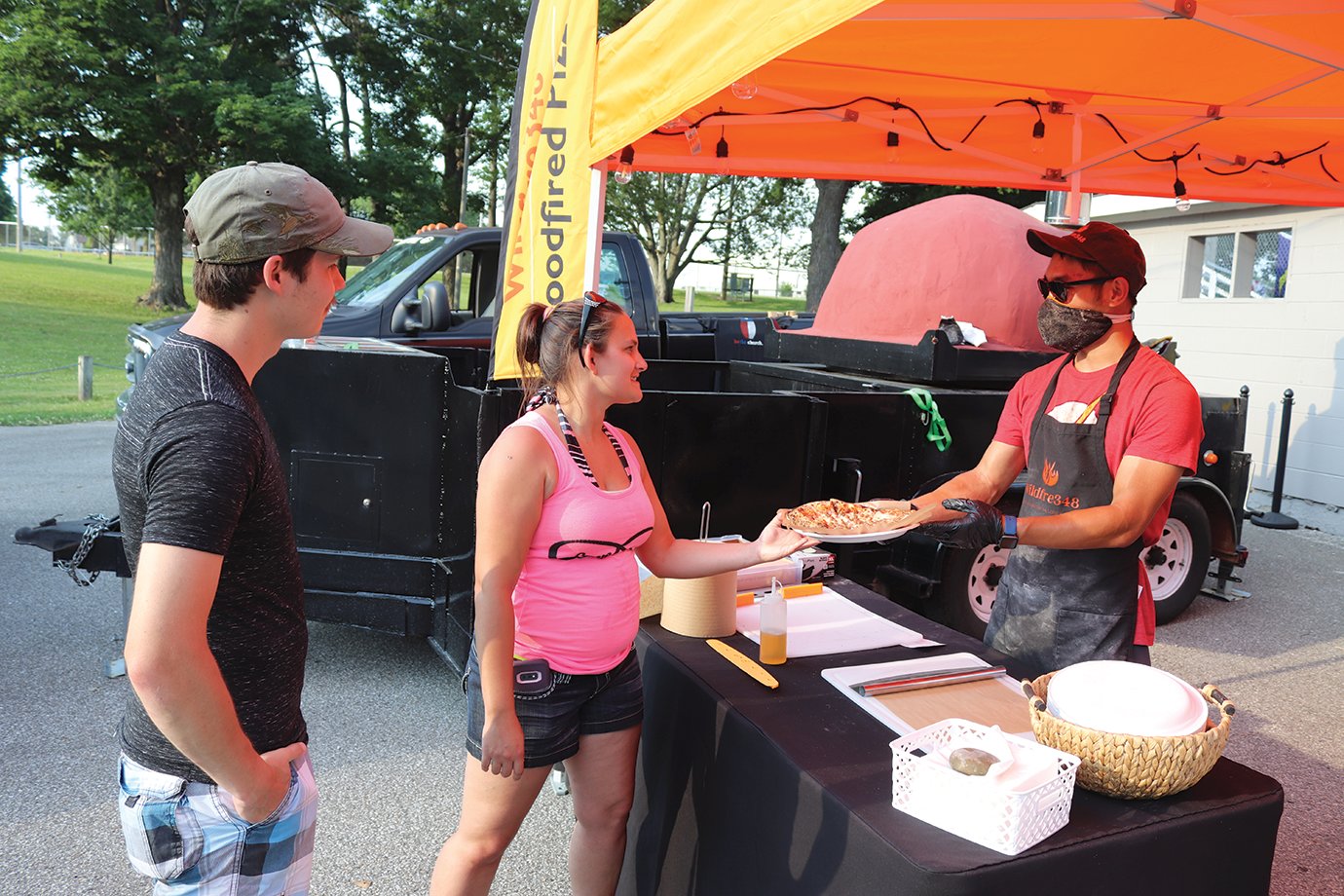 Waveland’s David Cotten, left, and Laura Lee Noel have their order filled by Wildfire 348’s Zach Green on Saturday at Milligan Park, which saw a fraction of attendants compared to previous years for Fourth of July celebrations.